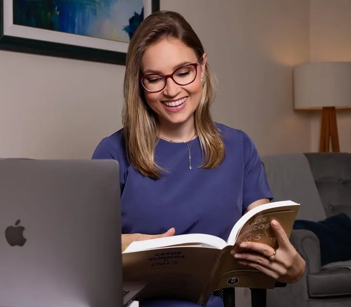 Aline Sá Copetti lendo um livro no consultório, sorrindo
